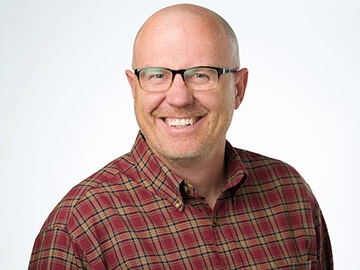 Christopher Phillips smiling and wearing a red plaid shirt and glasses.