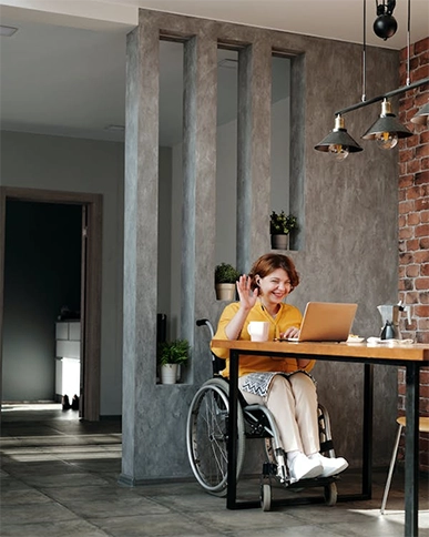 A woman in a wheelchair wearing headphones and using a laptop.