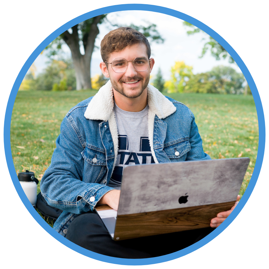 USU student sitting on grass with laptop smiling.