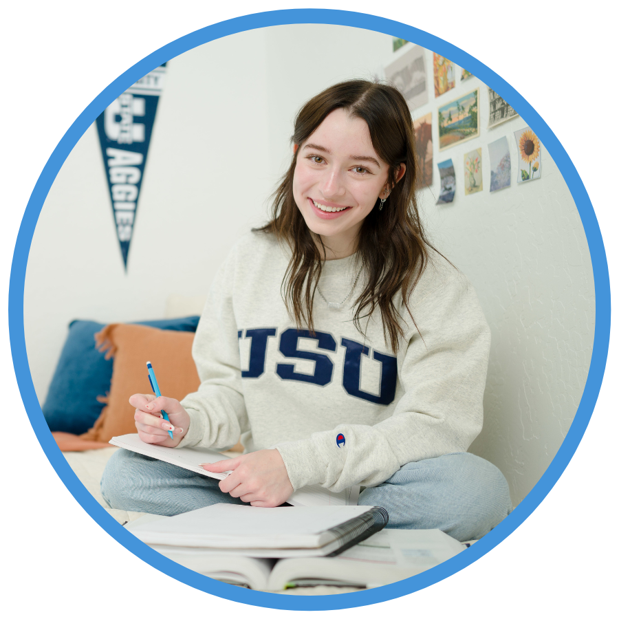 USU student sitting on their bed with a notebook.