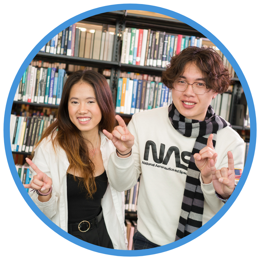Two international students at USU making the "Go Aggies" bull hand sign and smiling at camera.