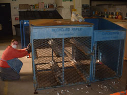 A volunteer kneels next to a piece of Recycling machinery
