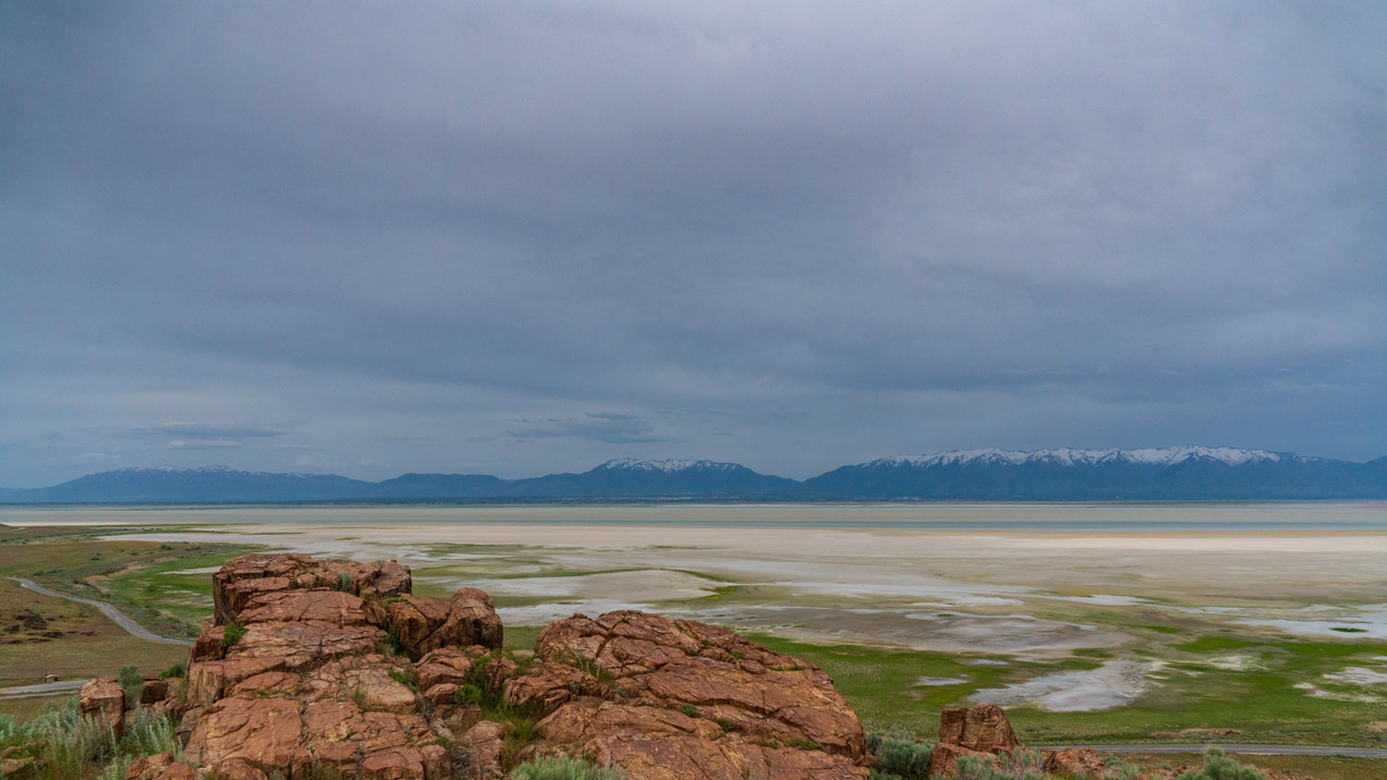 Plain with red rock in the foreground, mountains in the background, and an overcast sky