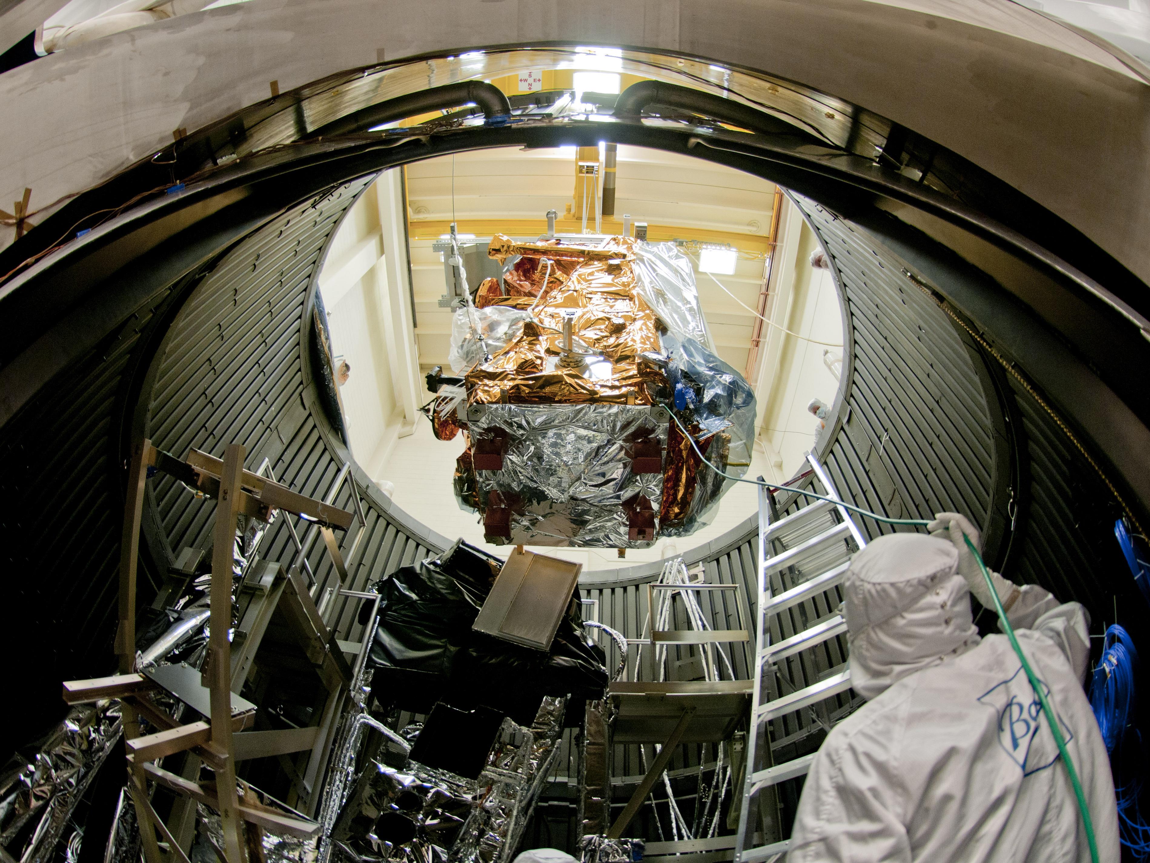 A group of engineers testing a satellite in a large chamber