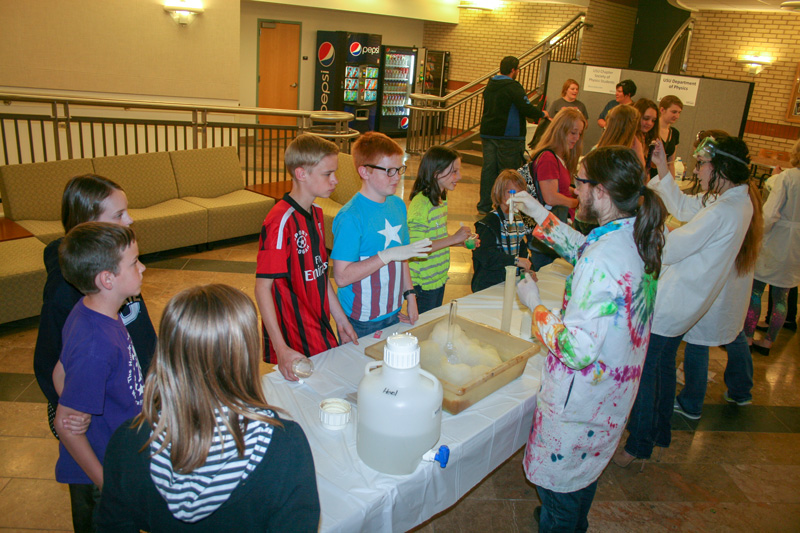Students gather around a long table of science displays