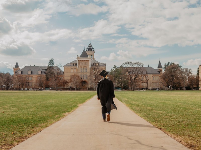 A USU graduate walks the sidewalk in front of Old Main