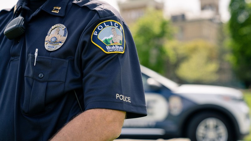 A USU Police Department officer stands in front of a patrol vehicle on campus.