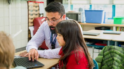 A teacher and a student using a laptop in a classroom.