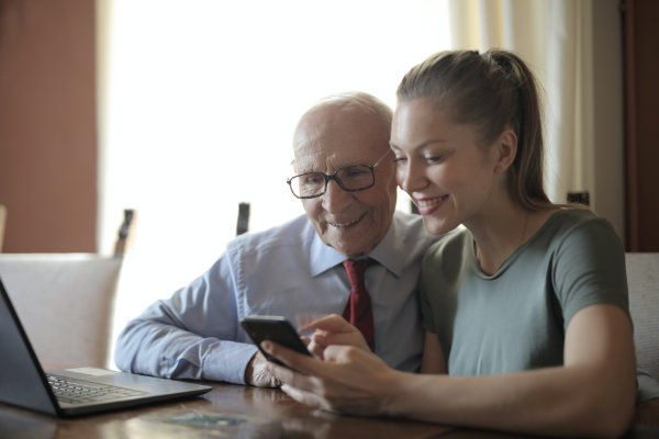 A young woman helps an elderly man with a smartphone